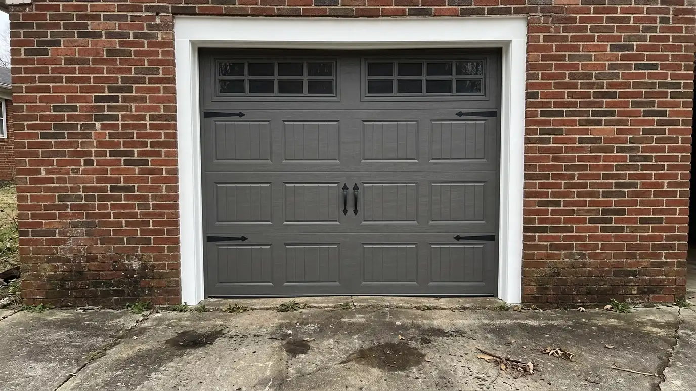 After: A worn old door replaced by a new insulated carriage-house style door | Music City Garage Door Service After: a front-facing garage with a new insulated charcoal carriage-house style door with small top windows and black handles