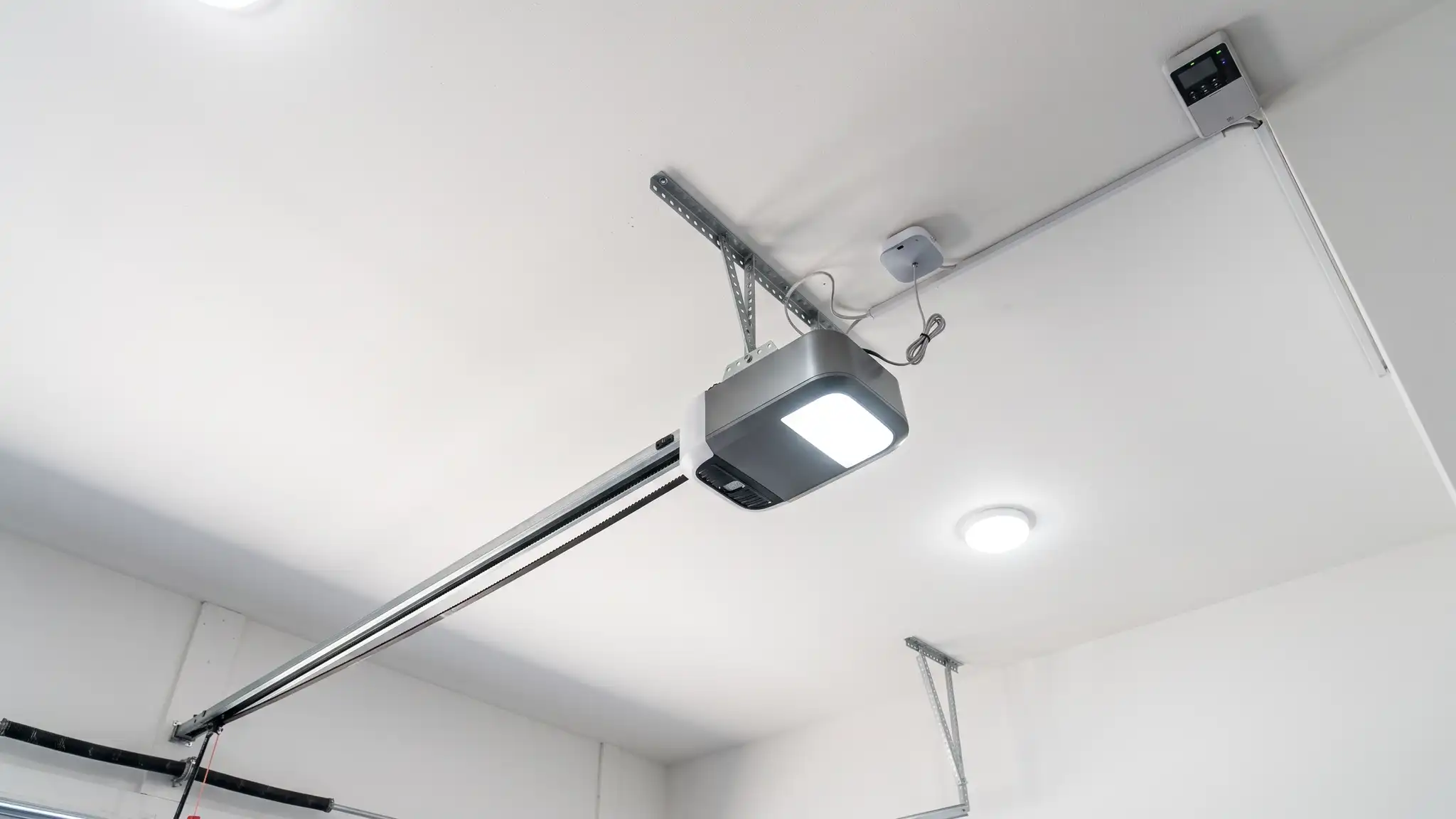 Openers and smart control | Music City Garage Door Service A clean white garage ceiling with a modern belt-drive garage door opener on a rail, a bright LED light and a wall-mounted control panel