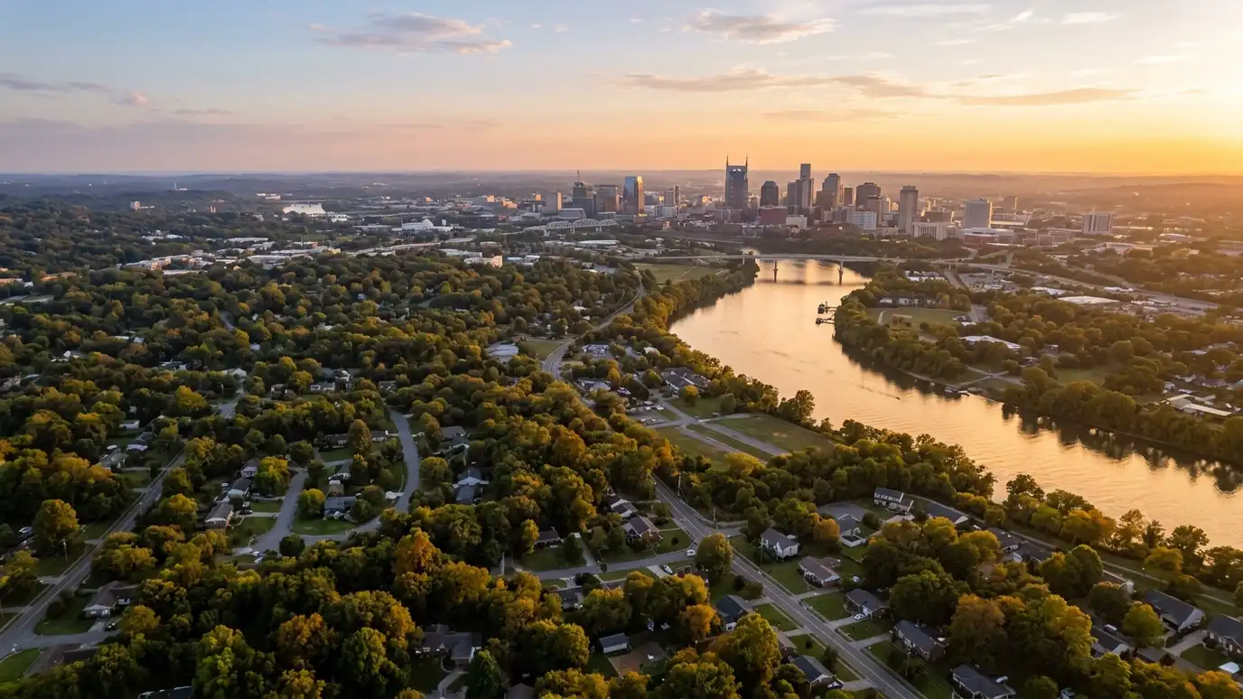 A golden sunset aerial view of the Nashville skyline above tree-covered suburban neighborhoods with a winding river